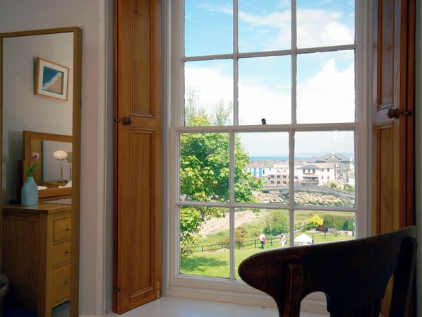 A room with a large window, wooden furniture, a mirror, and a framed picture on the wall.