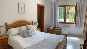 A neatly made bed with a wooden headboard, a bedside table with a lamp, a patterned rug, and a window with curtains. - FAMILY VILLA WITH POOL NEAR MORAIRA (Teulada)