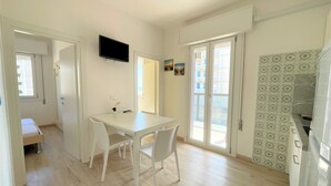 A compact kitchen with a white table, chairs, and a TV mounted above. - Ivana condo about 50mt from the sea in central area (Bibione)