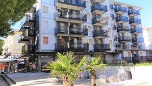 A multi-story residential building with balconies, air conditioning units, and a small palm tree in the foreground. - Ivana condo about 50mt from the sea in central area (Bibione)