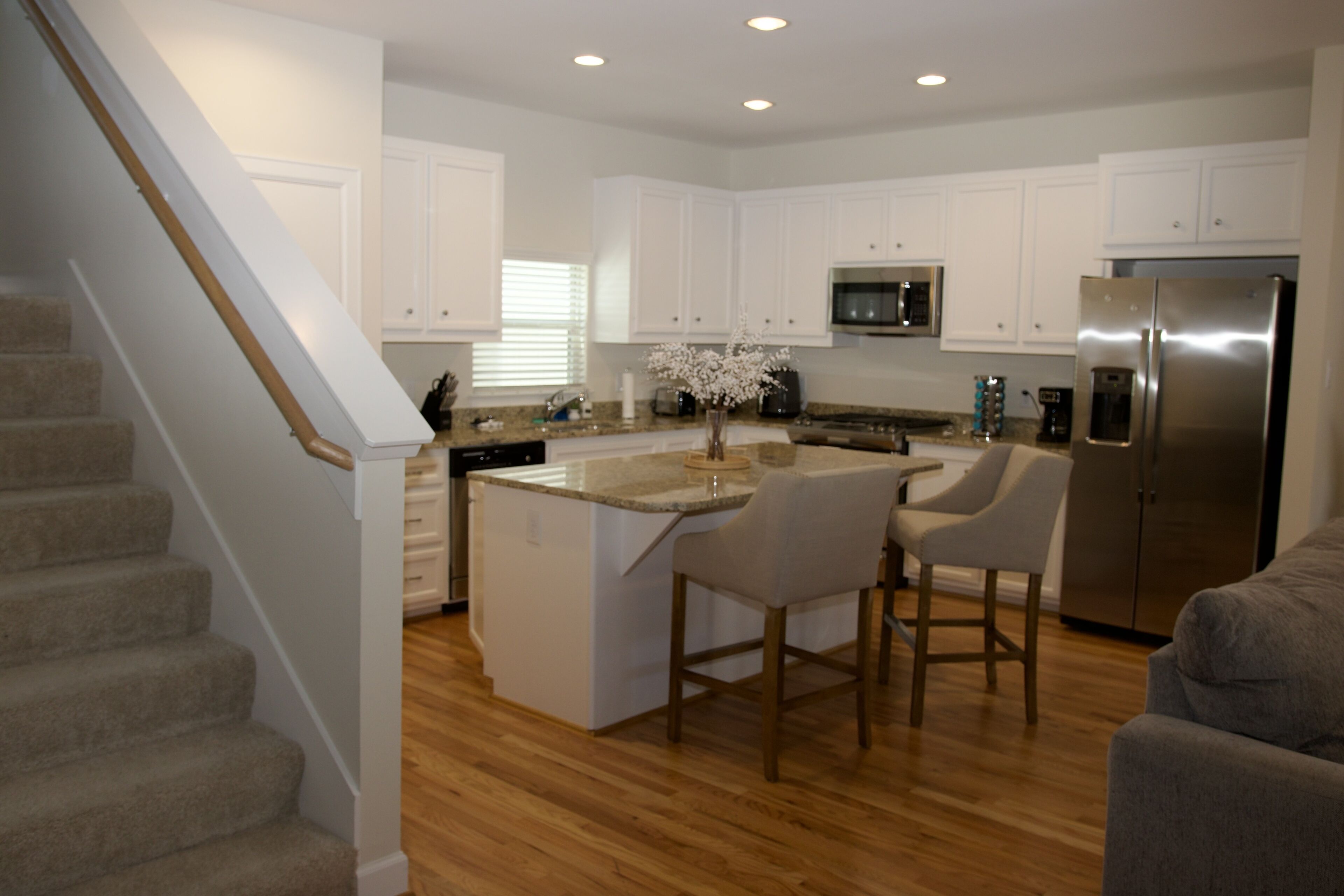 A modern kitchen with white cabinets, a stainless steel refrigerator, and a wooden island with bar stools.