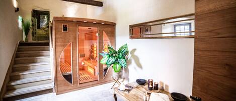A wooden staircase leading to a room with a glass door, a wooden table with towels and candles, and a potted plant.