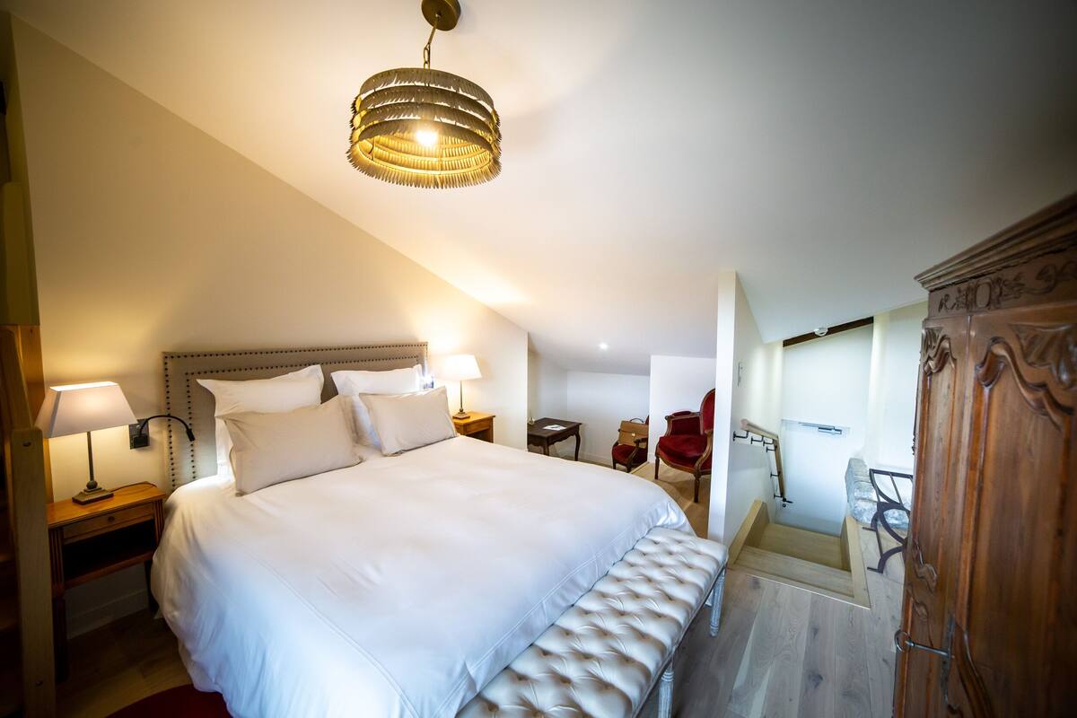 A hotel room with a large bed, bedside lamps, a wooden wardrobe, and a small desk with a chair.