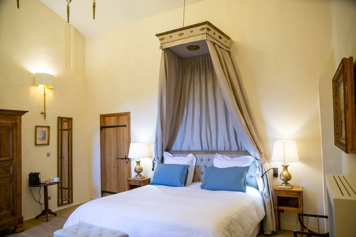 A bedroom with a four-poster bed, two bedside tables with lamps, a wooden wardrobe, and a framed picture on the wall.