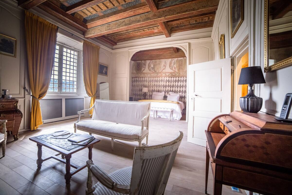 A room with a wooden ceiling, a white sofa, a small table, and a desk with a lamp.