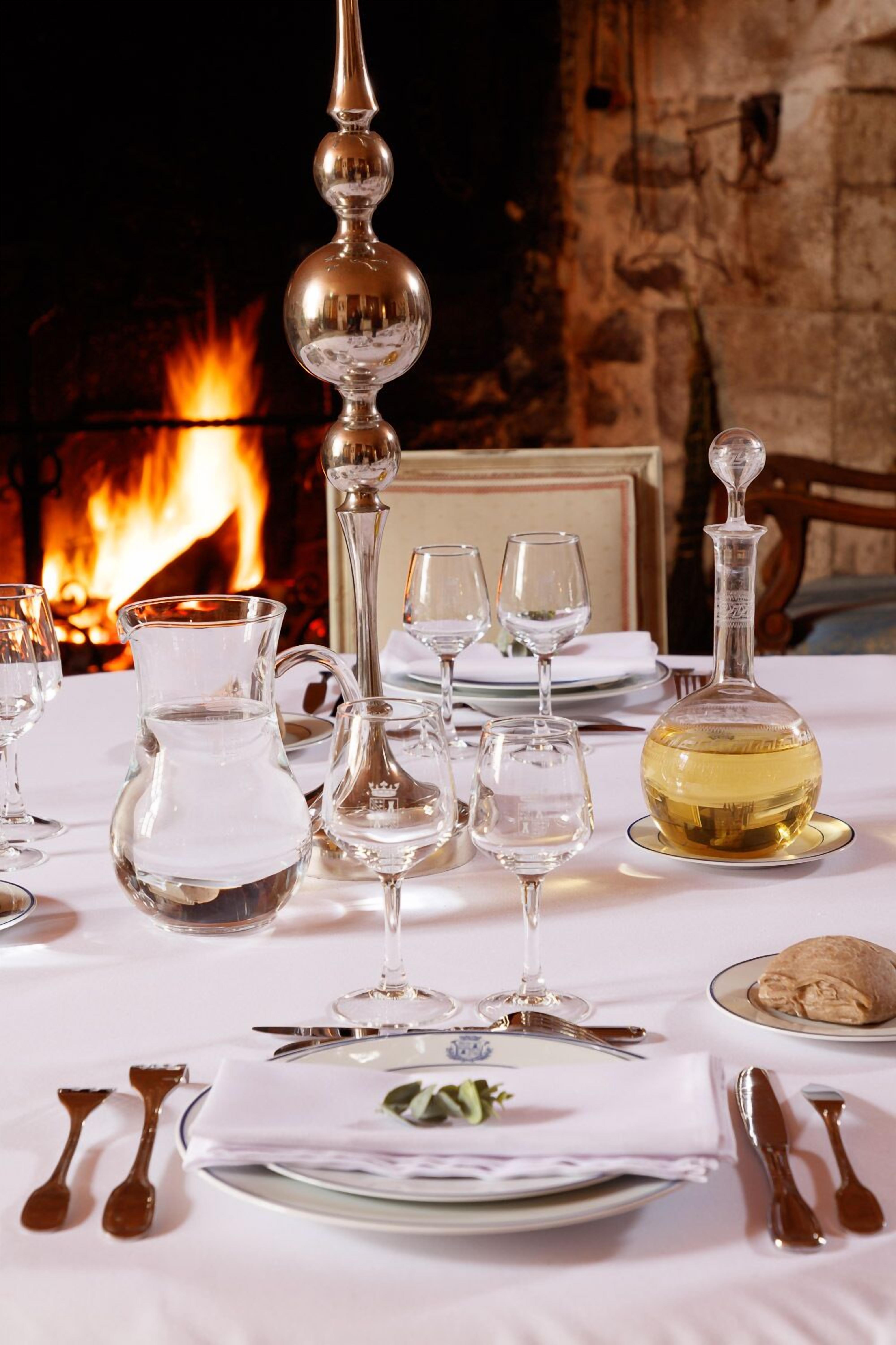 Una mesa de comedor dispuesta con cristalería y una botella de vino blanco, con una chimenea al fondo.
