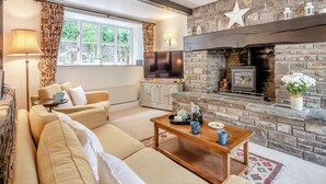 A cozy living room with a stone fireplace, a sofa, a coffee table, and a window with curtains.