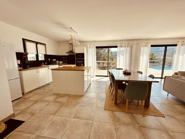 A modern kitchen with a central island, dining area with a table and chairs, and a view of a swimming pool through large windows. - Beautiful!!! Villa Cerise in southern Ardèche, Les Vans—private pool, stunning views (Les Vans)