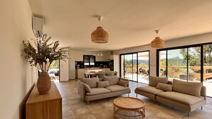 Amplia sala de estar con un ventanal, una cocina al fondo y un comedor con mesa y sillas.