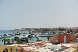 A marina with boats docked, a cityscape in the background, and a building with a distinctive arched entrance.