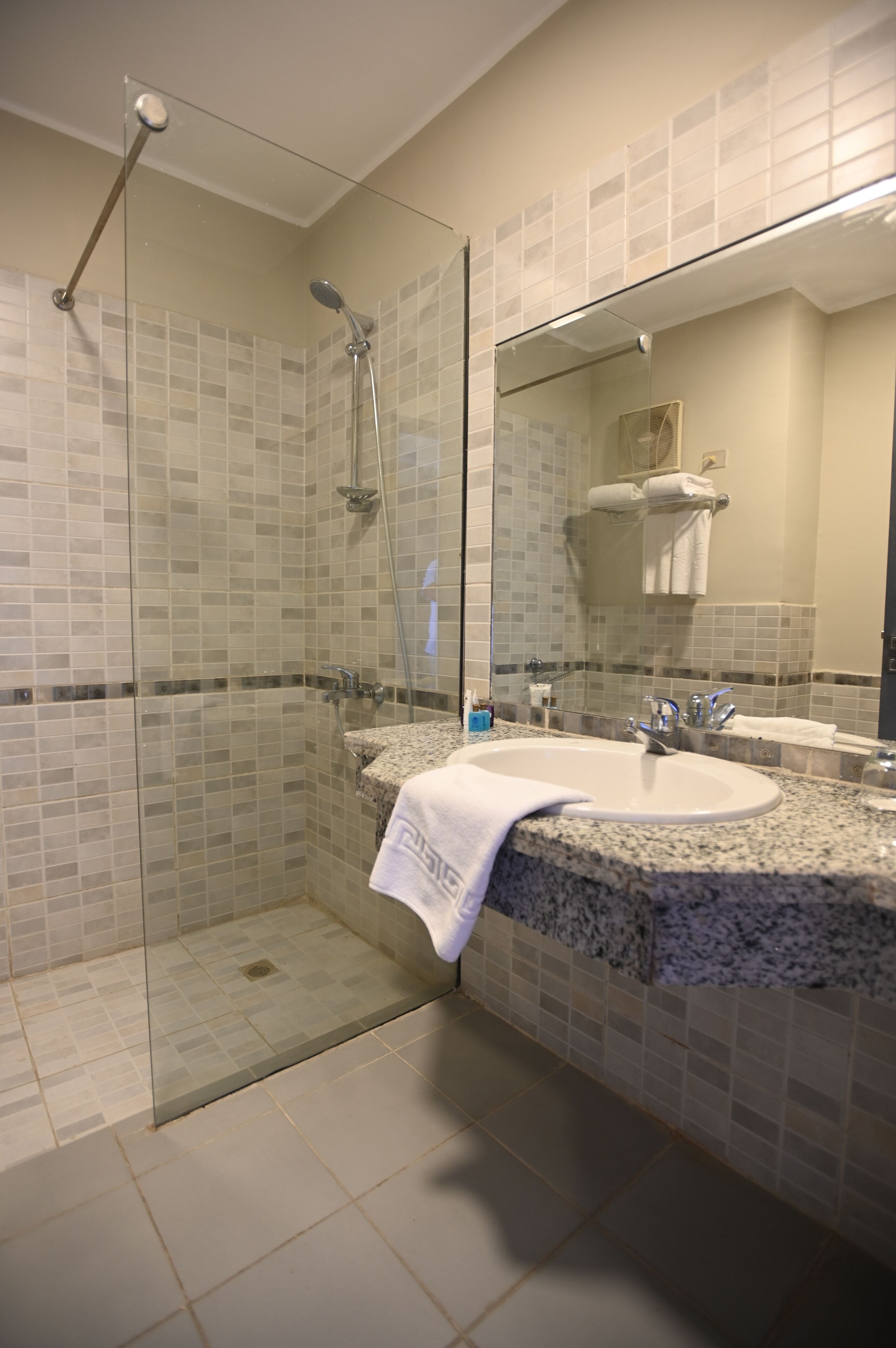 Un baño con ducha envuelta en vidrio, lavamanos de encimera de granito y un espejo grande.