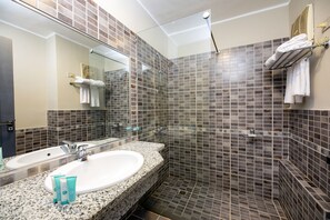 A bathroom with two sinks, a glass shower enclosure, and a tiled shower wall.