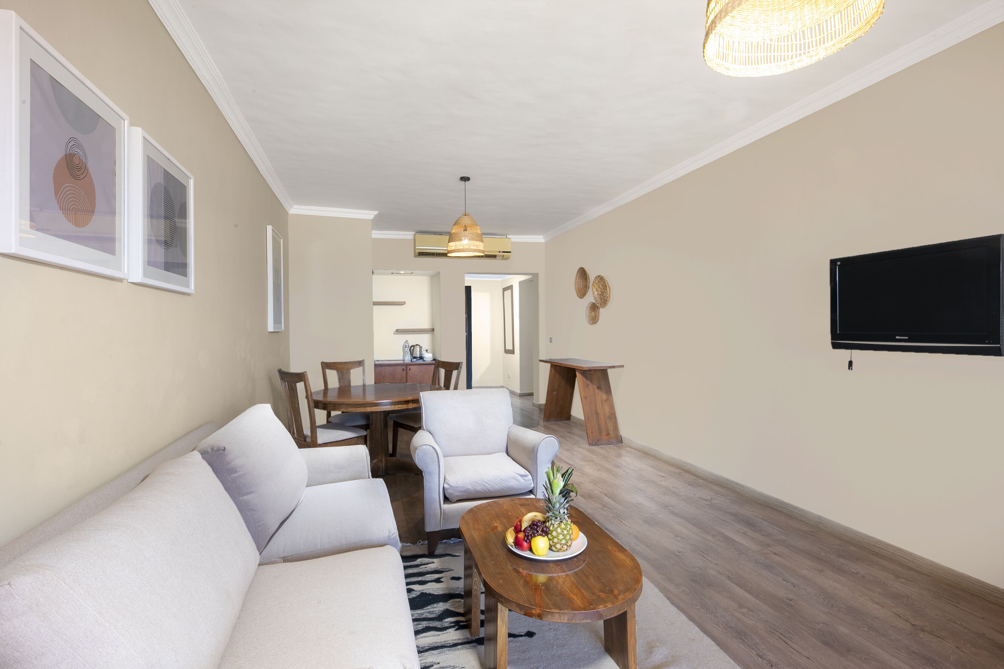 Una sala de estar moderna con un sofá, sillones, una mesa de centro con fruta, un comedor y un televisor montado en la pared.