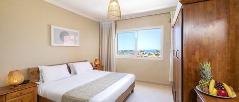 Un dormitorio con cama, lámparas de noche, armario, frutero, ventana con vistas y luz de techo.
