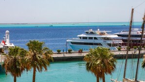 Un port de plaisance où est amarré un grand yacht, avec des palmiers et des eaux turquoise et calmes.