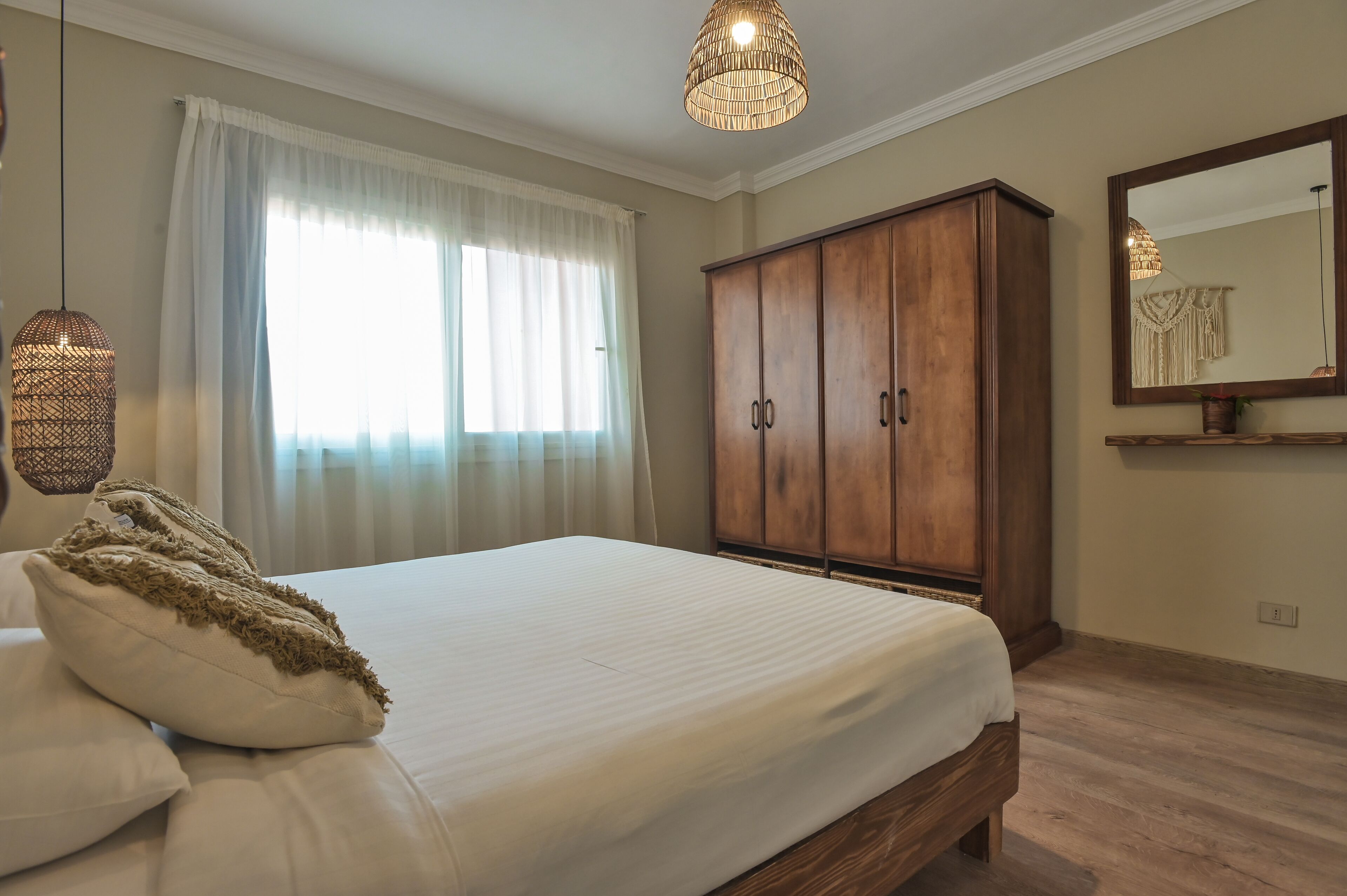 A bedroom with a bed, a wardrobe, a hanging light fixture, and a window with curtains.