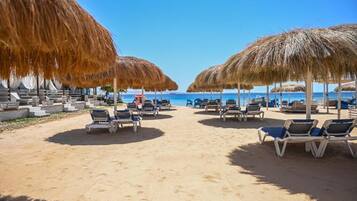 A beach with rows of sun loungers and thatched umbrellas, leading to the sea.