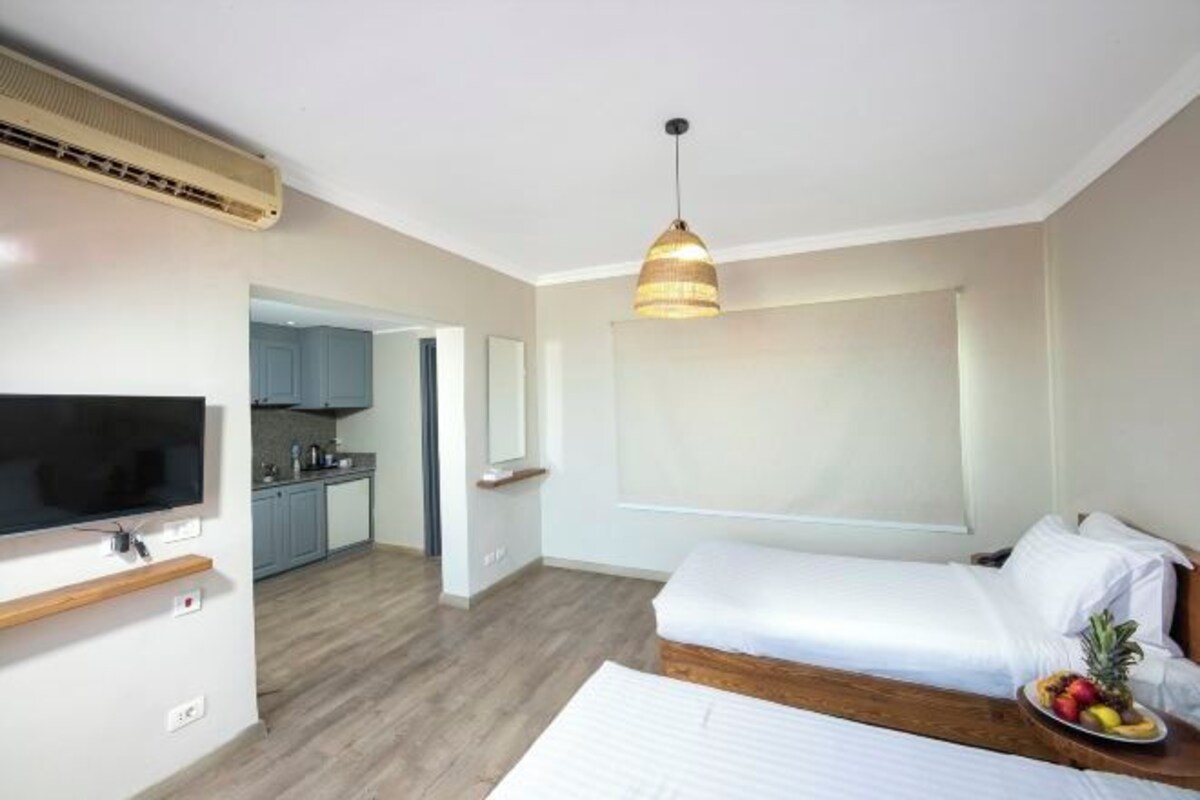 Een hotelkamer met een bed, een televisie, een keukenhoek en een schaal met fruit.