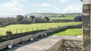 A stone wall with potted plants, a grassy field, and a distant view of houses and hills. - 3 bedroom accommodation in Aberdaron (Aberdaron)