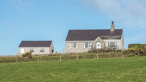 Two houses with a grassy field in front, one with a stone facade and the other with a plain wall. - 3 bedroom accommodation in Aberdaron (Aberdaron)