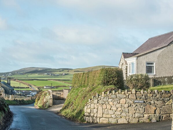 A stone wall with a sign reading "BRYN CRUG" and a house with a stone facade and a pitched roof.