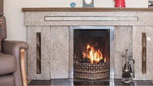 A fireplace with a fire, a clock, and a vase of flowers on the mantel. - 3 bedroom accommodation in Aberdaron (Aberdaron)