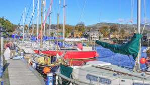 A marina with multiple boats docked, a wooden pier, and a backdrop of hills. - Bwthyn Stabal-QC1199 (Criccieth)