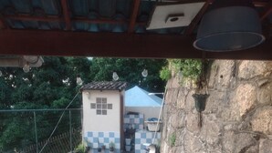 Une piscine rectangulaire bordée de carreaux, entourée d’un mur de pierre et d’une terrasse en bois. On y trouve des chaises en plastique blanches et une petite table sur la terrasse.