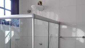 Une salle de bain moderne avec une douche à l’italienne en verre, des murs recouverts de carreaux blancs et une fenêtre visible.