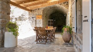 A stone-walled outdoor dining area with wooden furniture and potted plants. - Château de Laulagnet - 3e avec piscine dans un écrin de verdure (Jaujac)