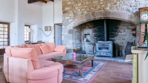 A cozy living room with a stone fireplace, a pink sofa, and a wooden coffee table. - Château de Laulagnet - 3e avec piscine dans un écrin de verdure (Jaujac)