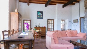 A rustic interior with a wooden dining table, a pink sofa, and a stone wall. - Château de Laulagnet - 3e avec piscine dans un écrin de verdure (Jaujac)
