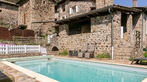 A stone building with a swimming pool, outdoor seating, and a white fence. - Château de Laulagnet - 3e avec piscine dans un écrin de verdure (Jaujac)