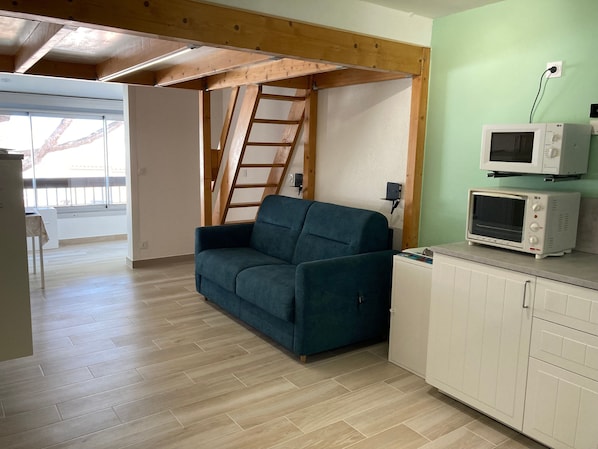 A room with a wooden ceiling, a blue sofa, a white cabinet, and a microwave.