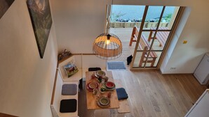 A dining area with a wooden table set for four, a hanging light fixture, and a view of an outdoor deck through a glass door. - Wellnesshof Müller Vorderburg (Rettenberg)