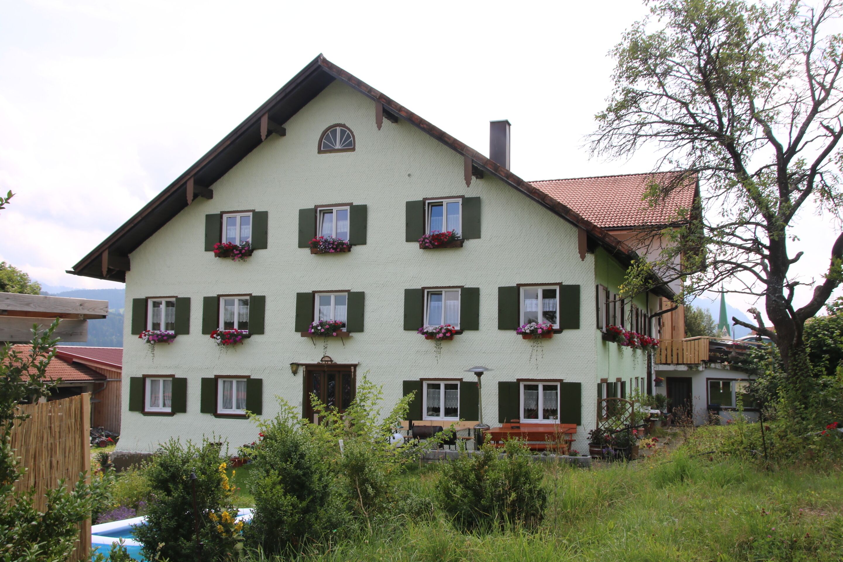 Ein mehrstöckiges Gebäude mit grünen Fensterläden, einem geneigten Dach und Blumenkästen an den Fenstern.