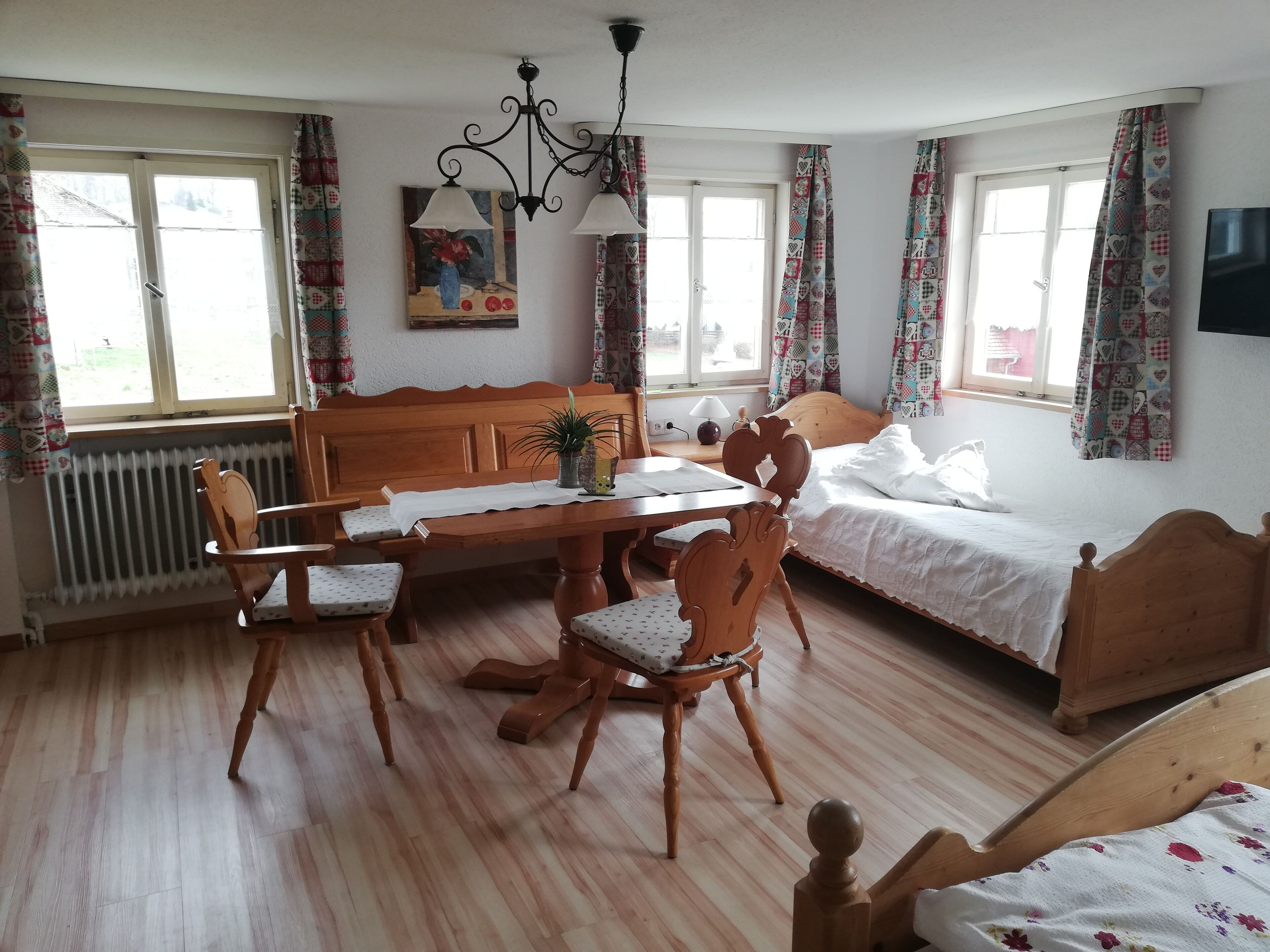 A cozy room with a wooden dining table, chairs, a bed, and a radiator.