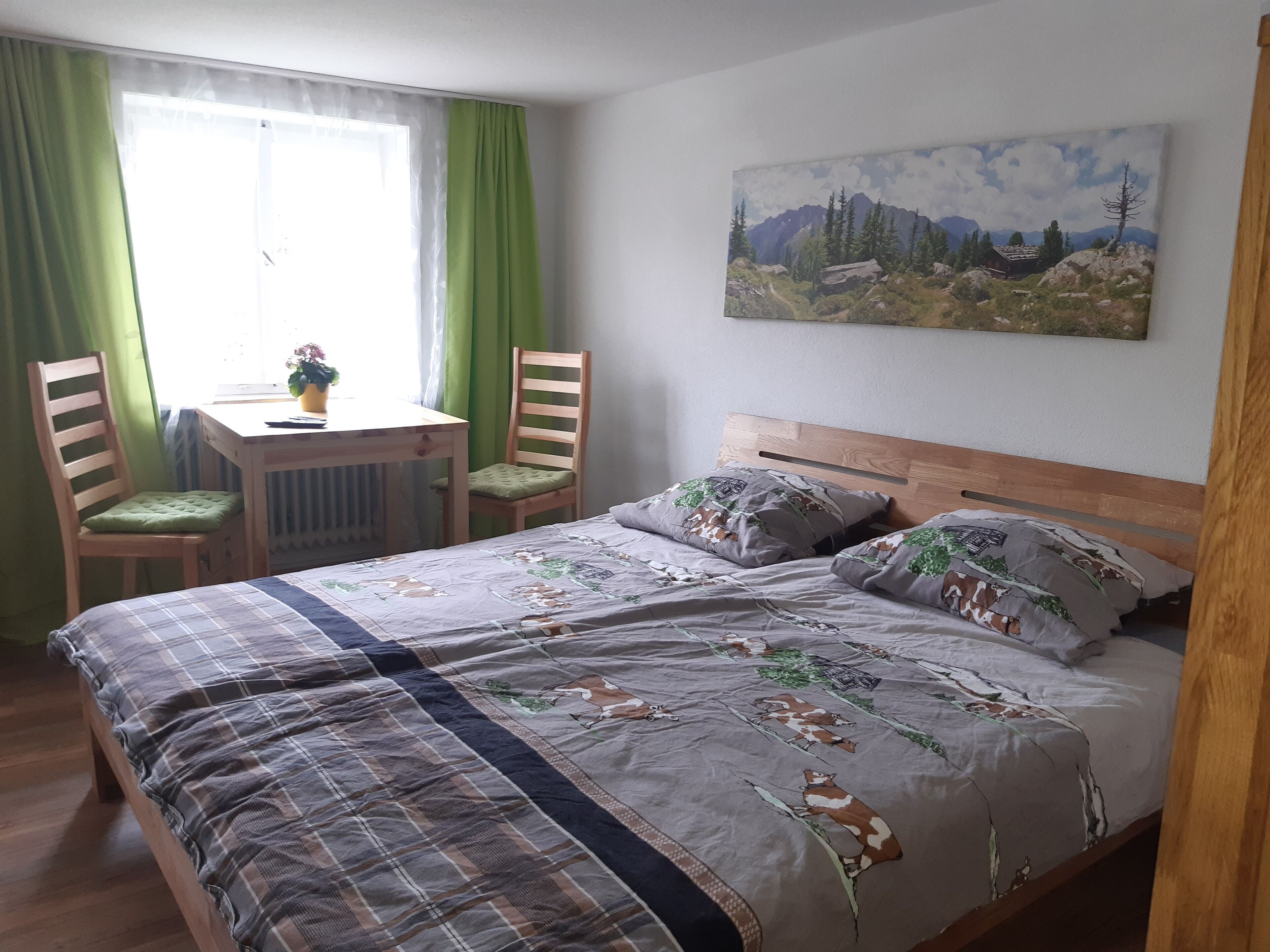 A bedroom with a bed, two chairs, a small table, and a painting on the wall.