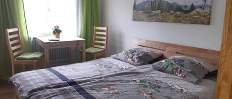 A bedroom with a bed, two chairs, a small table, and a painting on the wall.