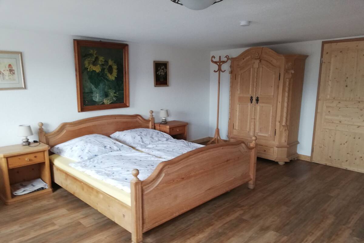 A wooden bed with a headboard, a nightstand, a lamp, a wardrobe, and a painting on the wall.