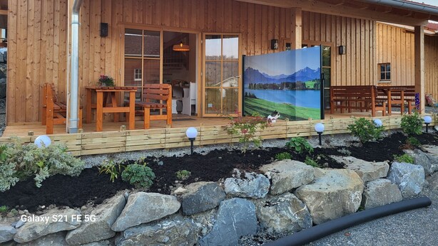 A wooden cabin with a covered porch, a dining area, and a scenic painting. - Wellnesshof Müller Vorderburg (Rettenberg)