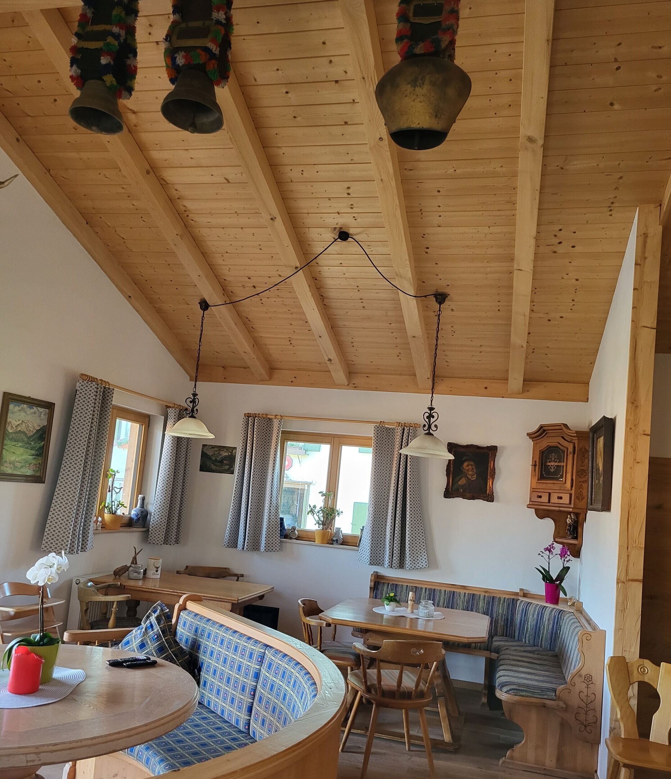 A wooden interior with a high ceiling, multiple windows, and a variety of seating arrangements including a round table and a bench.