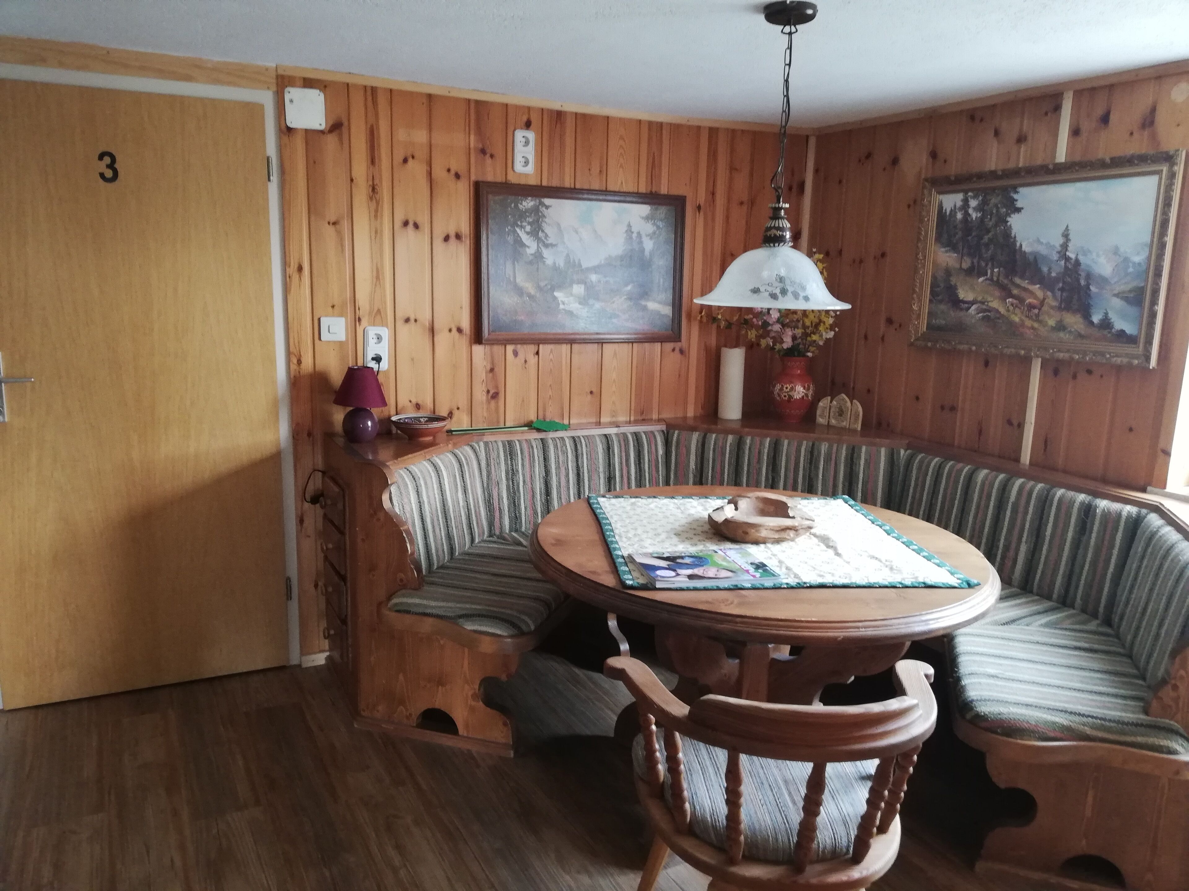 A cozy room with a wooden wall, a round table with a placemat, a cushioned bench, and a chair.