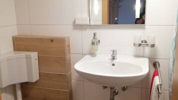Un baño con lavamanos blanco, un espejo, un inodoro con tapa azul y un cubo de basura.