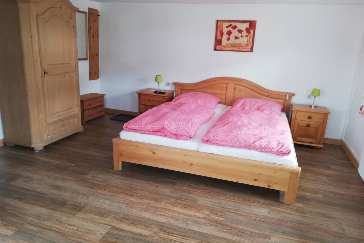 A bedroom with a wooden bed, two bedside tables with lamps, a wooden wardrobe, and a framed picture on the wall.