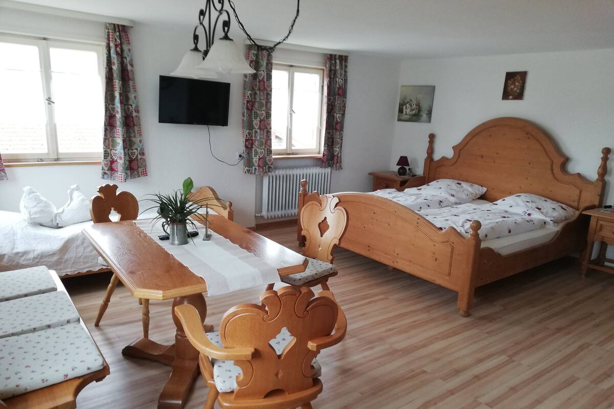 A bedroom with a wooden bed, a desk with a chair, a TV mounted on the wall, and a radiator.