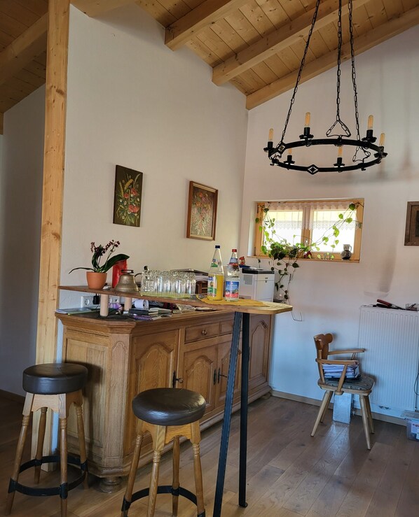 Cocina rústica con vigas de madera, barra con taburetes y una lámpara colgante.