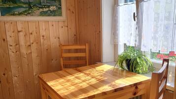 A wooden dining table with chairs, a hanging light fixture, a window with curtains, and a painting on the wall.