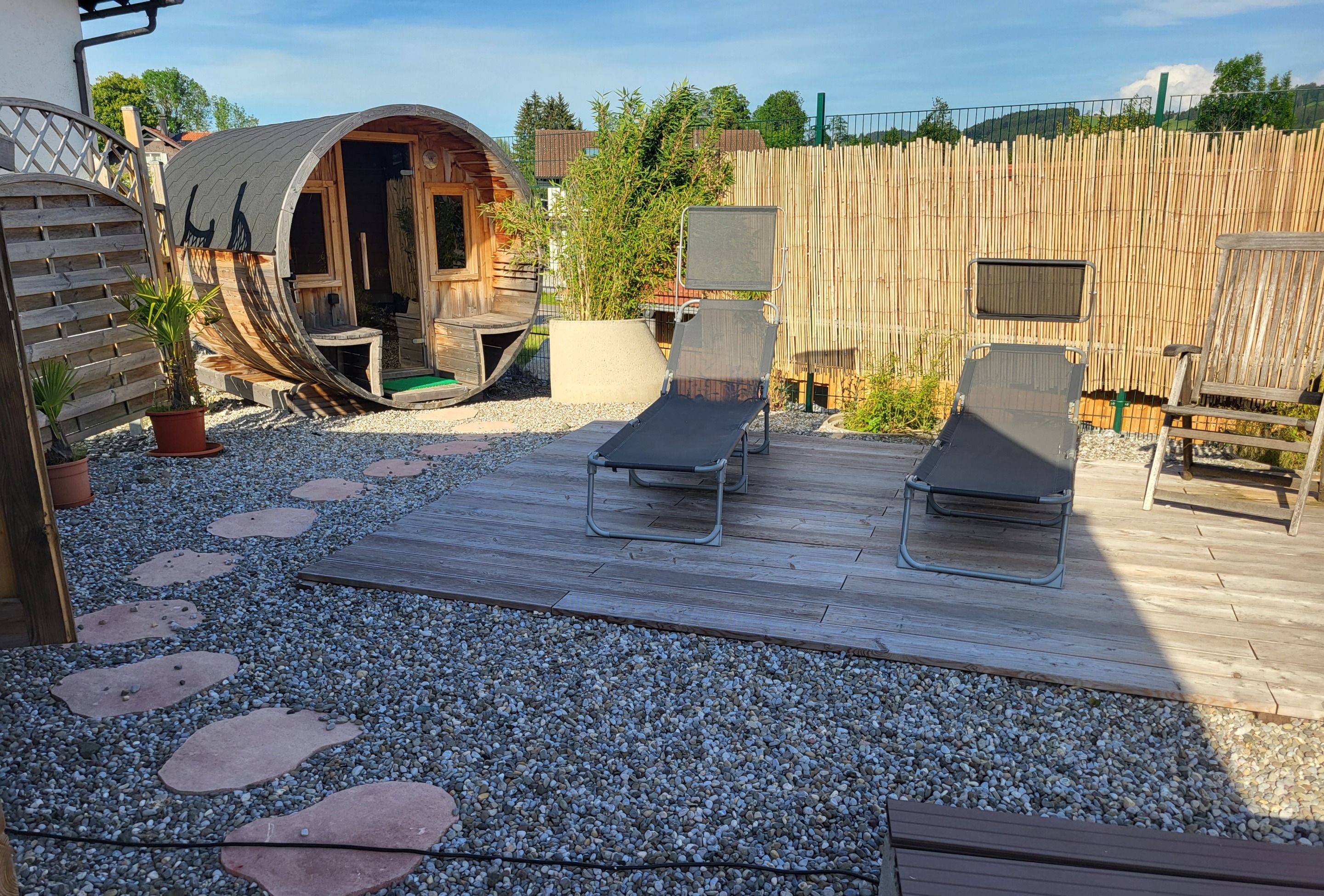 A patio area with a wooden deck, two lounge chairs, a small wooden structure, and a bamboo fence.