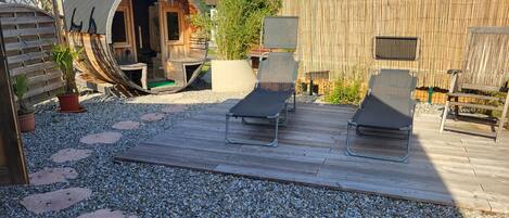 A patio area with a wooden deck, two lounge chairs, a small wooden structure, and a bamboo fence.